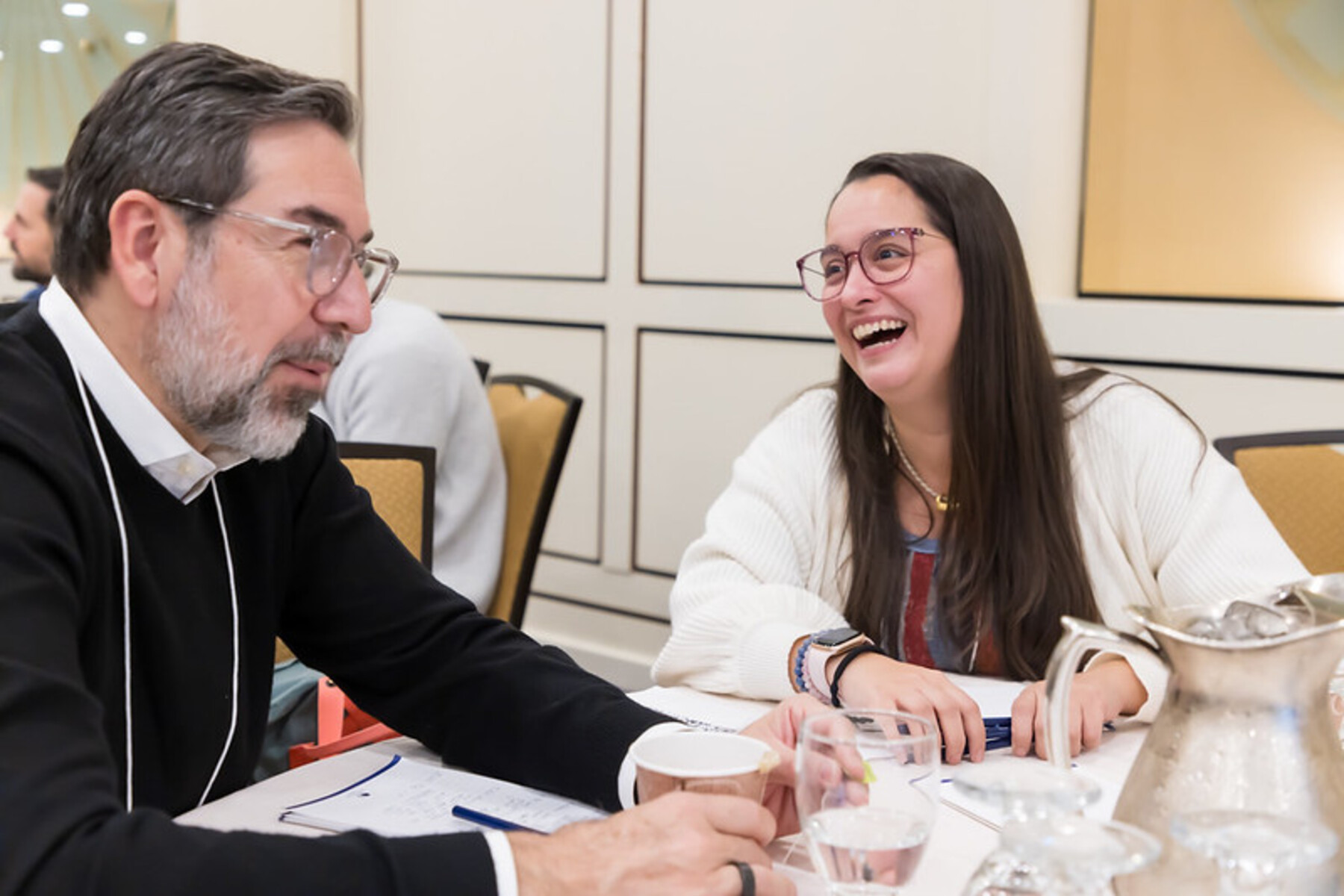 A man and woman laugh at a breakfast table during a conference