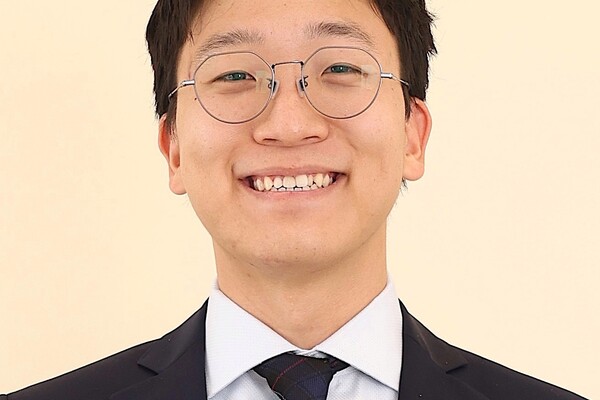 Dr. Alex Bak smiles against a pale yellow background.