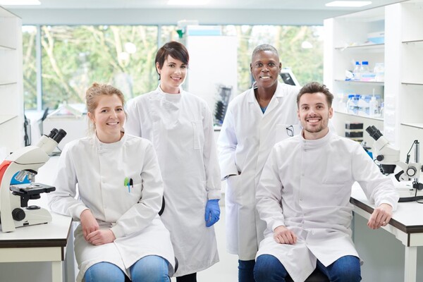 Stock photo. Four researchers pose in lab coats in a clean, white lab.