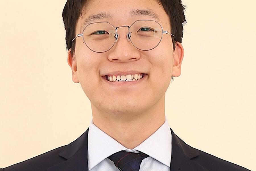 Dr. Alex Bak smiles against a pale yellow background. 