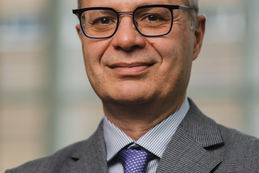 Dr Keyvan Karkouti wears a grey suit and purple tie. His arms are folded across his chest.
