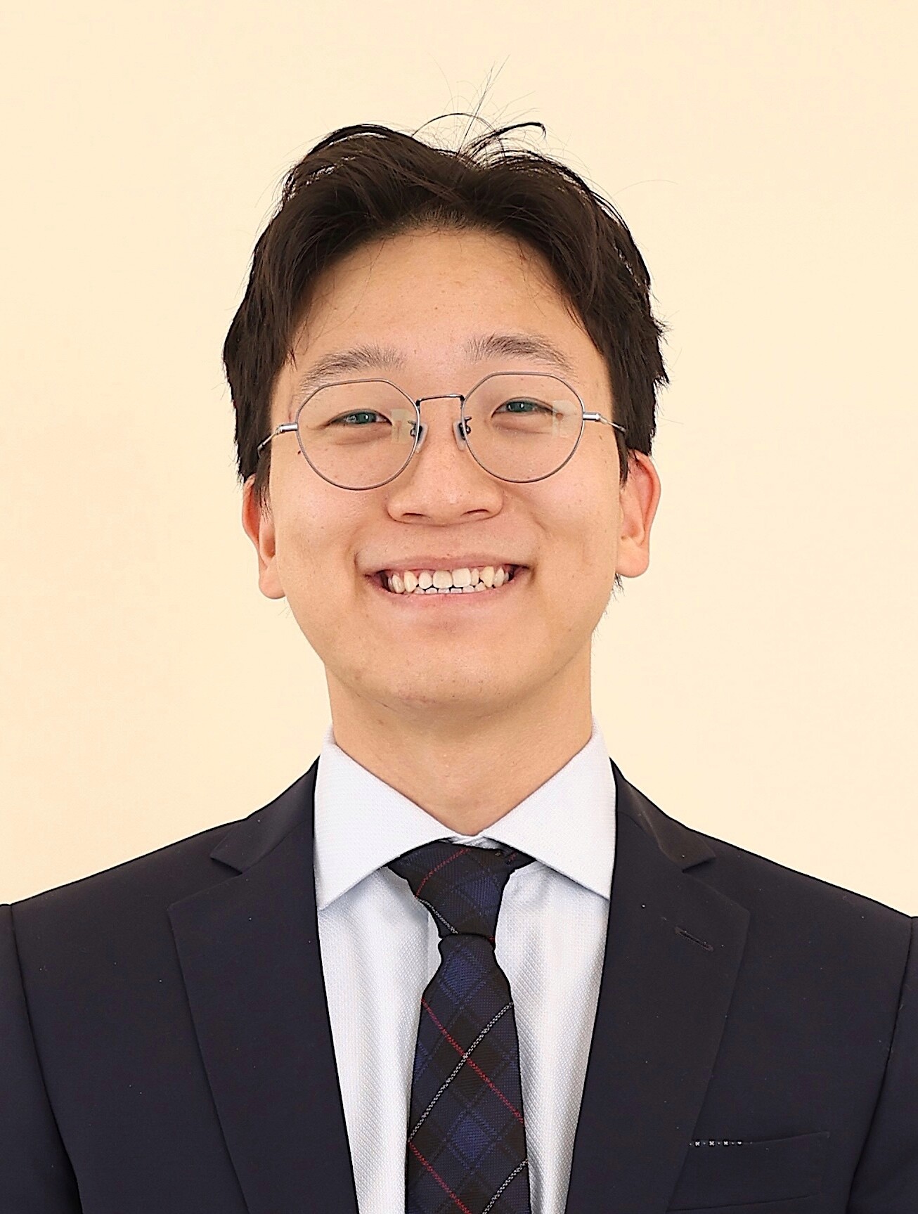 Dr. Alex Bak smiles against a pale yellow background. 