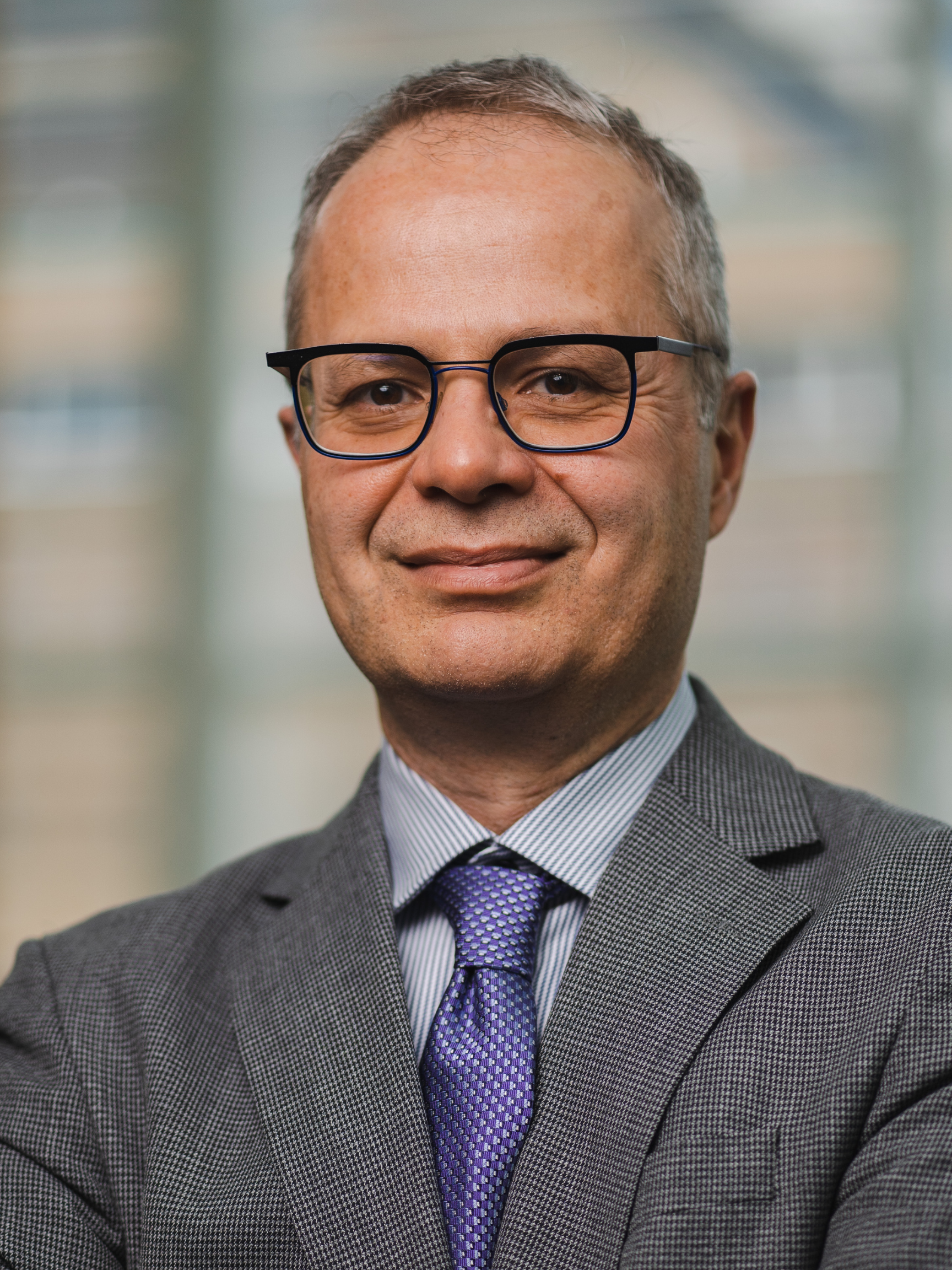 Dr Keyvan Karkouti wears a grey suit and purple tie. His arms are folded across his chest.