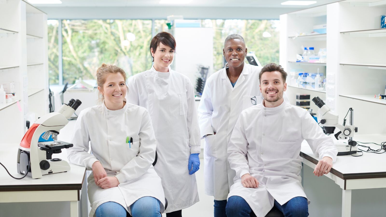 Stock photo. Four researchers pose in lab coats in a clean, white lab.