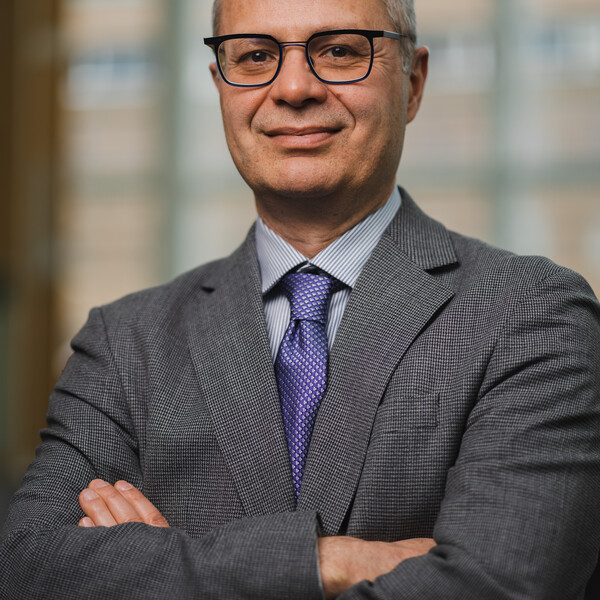 Dr. Keyvan Karkouti in a grey suit and purple tie against the bluured background of a hospital site